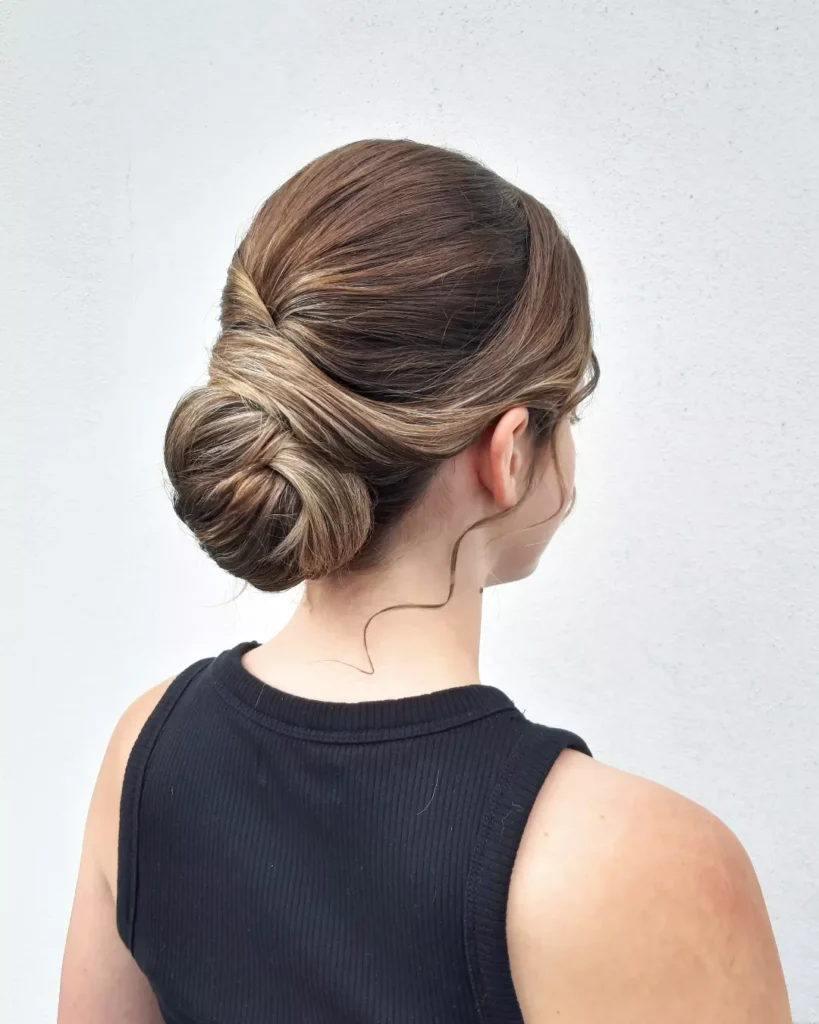 A woman with dark brunette hair styled in a thick and intricate low horizontal braid at the nape of her neck.