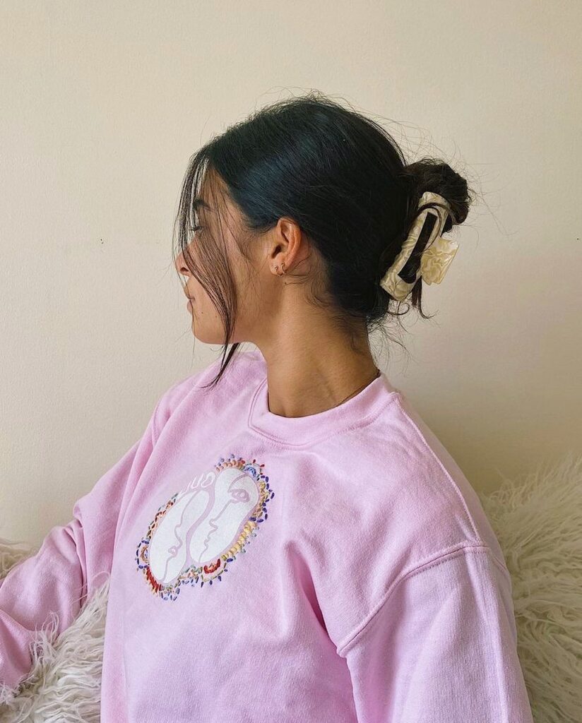 A woman with dark hair wears a messy low bun secured by a large cream claw clip with loose strands framing her face.