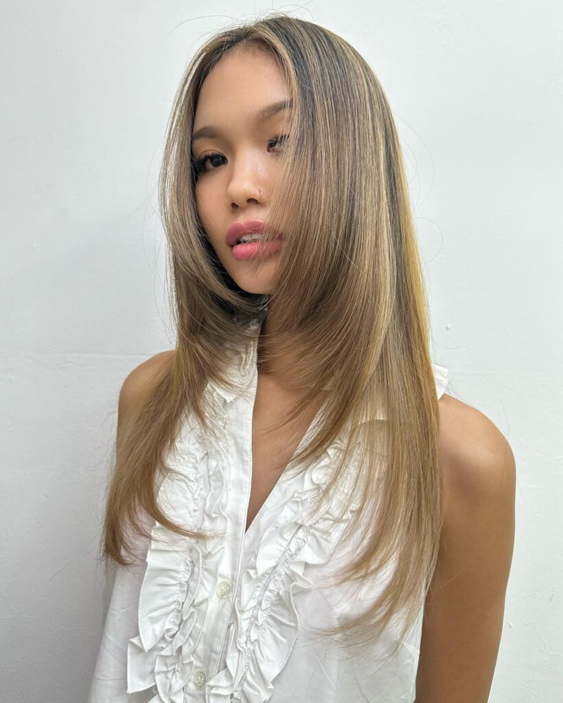A woman with long straight honey blonde hair featuring sharp face framing layers and sandy highlights.