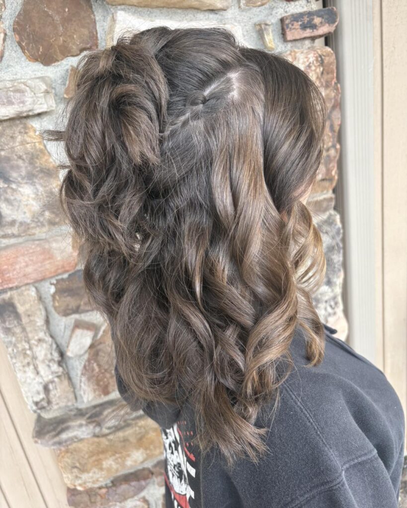 A woman with medium-length dark brown curly hair featuring a small accent braid on the side and voluminous textured layers.