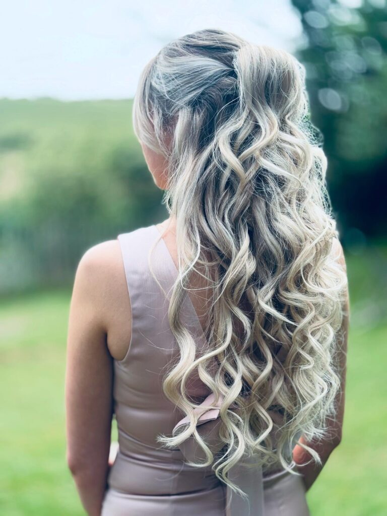 Long blonde curly hair styled in a half up high ponytail with loose curls cascading down the back.