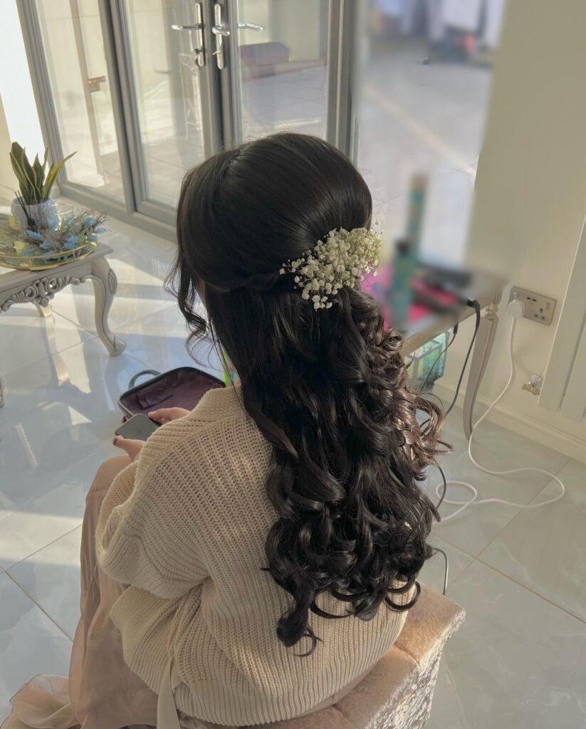 Long dark curly hair styled half up with a small floral accessory on the side.