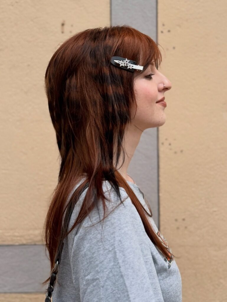 A woman with a long layered auburn shag haircut and a star hair clip pinning back her bangs.