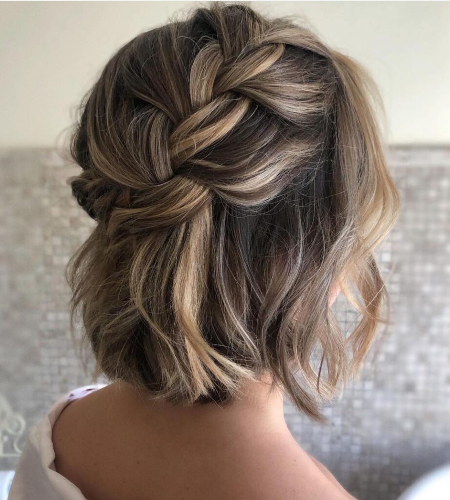 A woman with dimensional blonde and brunette hair styled with a dutch braided crown flowing into loose beachy waves.