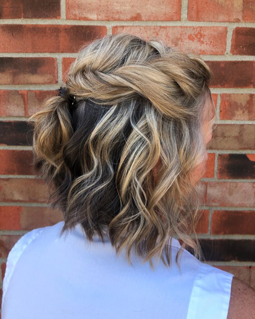 A woman with dimensional blonde highlights wears a half up twisted ponytail with loose beachy curls.