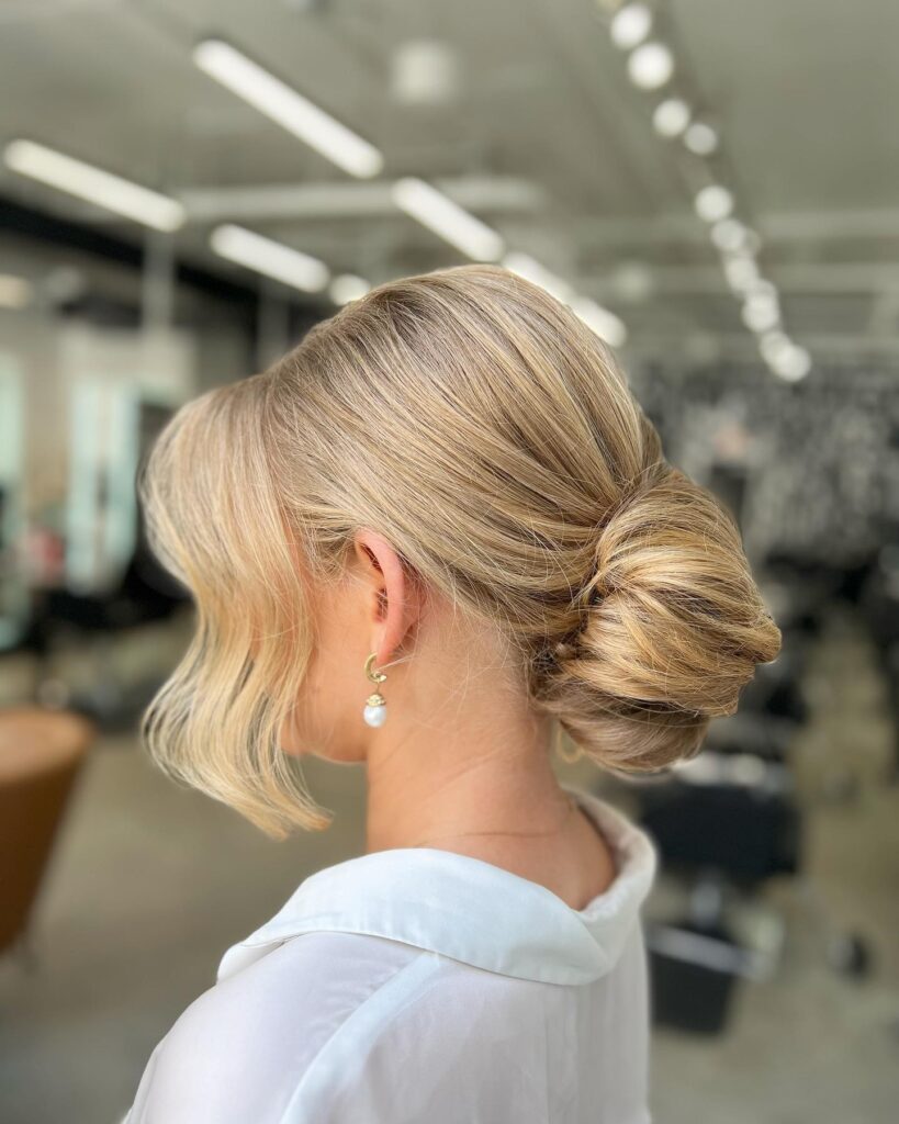 A woman with sleek golden blonde hair styled into a smooth low bun at the nape of her neck.