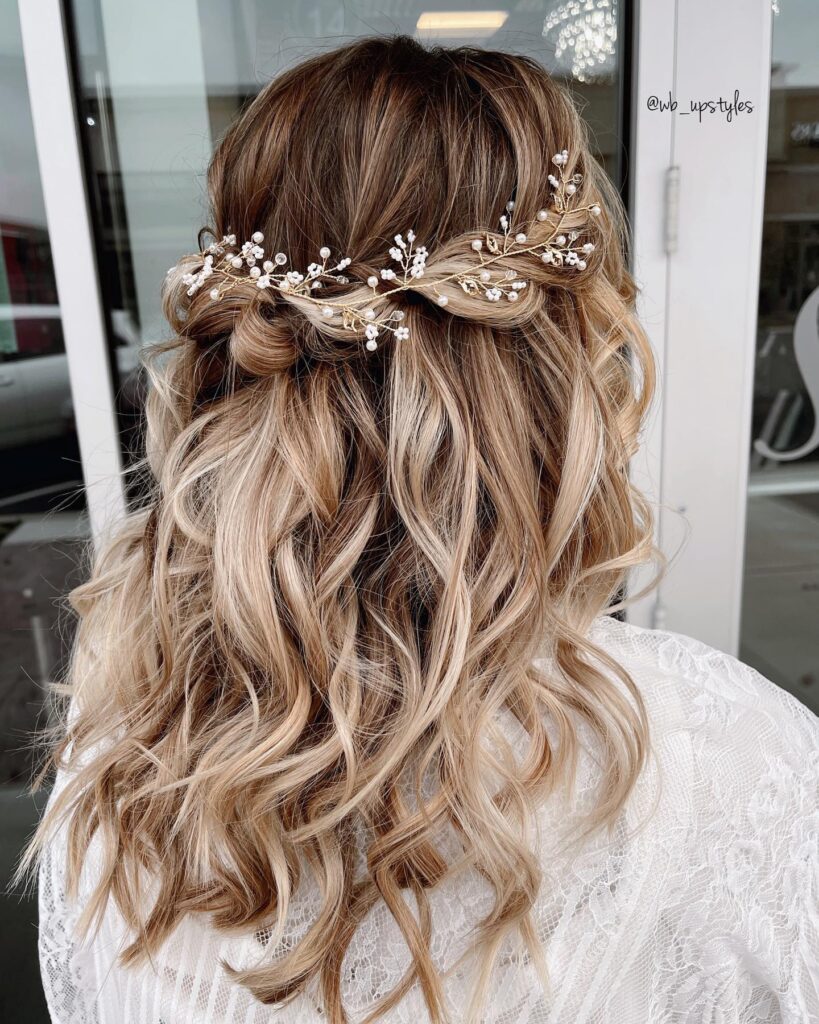 A woman with blonde balayage hair wears half up twists topped with a pearl vine and cascading curls.