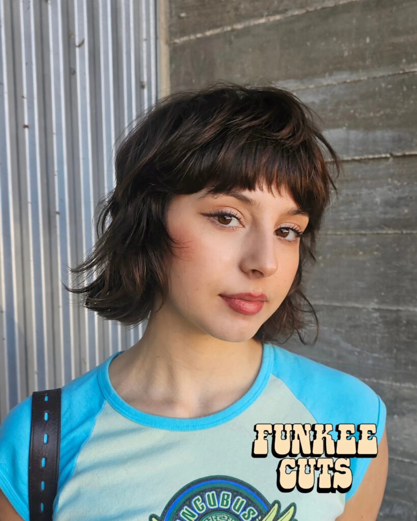 A woman with a chin length brunette bob shag featuring short choppy micro bangs.