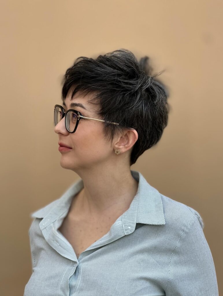 A woman with a voluminous salt and pepper pixie cut and glasses looks off to the side.