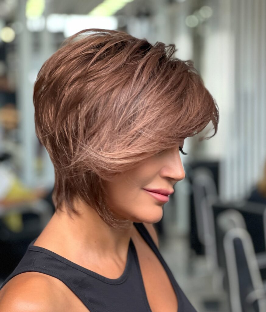 A woman with a feathered copper brown shag haircut and long side swept bangs looks down and to the side.