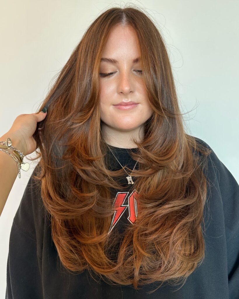 Long copper brown hair styled in soft layers with curled under, rounded ends.