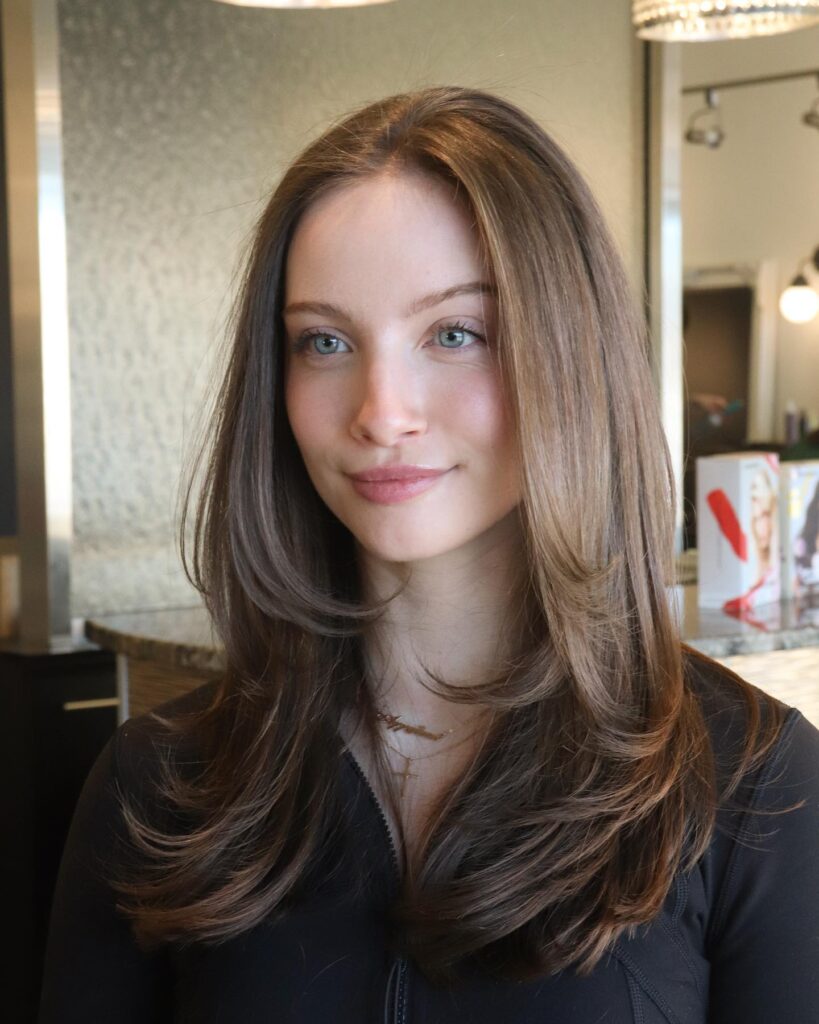 Medium brown hair with golden highlights styled in soft center-parted layers with flipped ends.