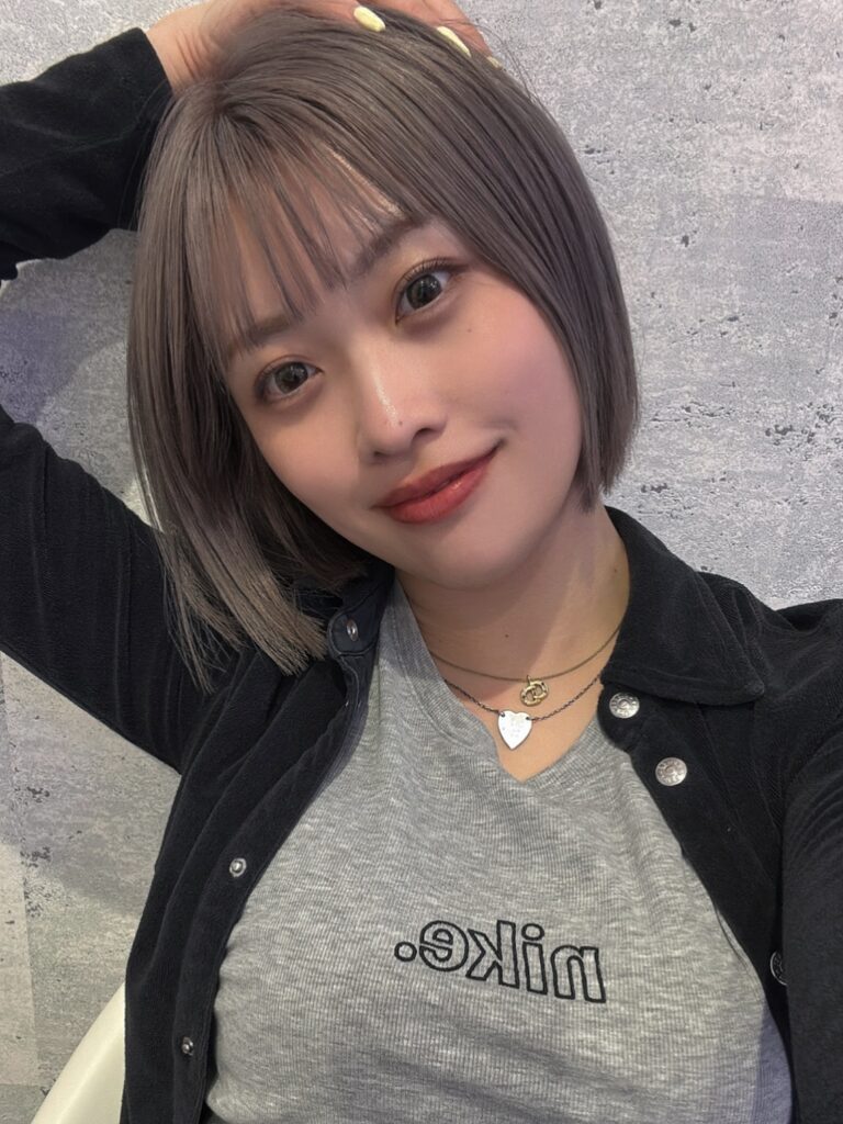 A woman with a sleek chin length ash brown bob and blunt full bangs.
