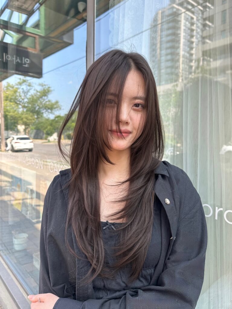 A woman with long dark brown hair featuring a heavy side swept fringe and soft, airy layers.