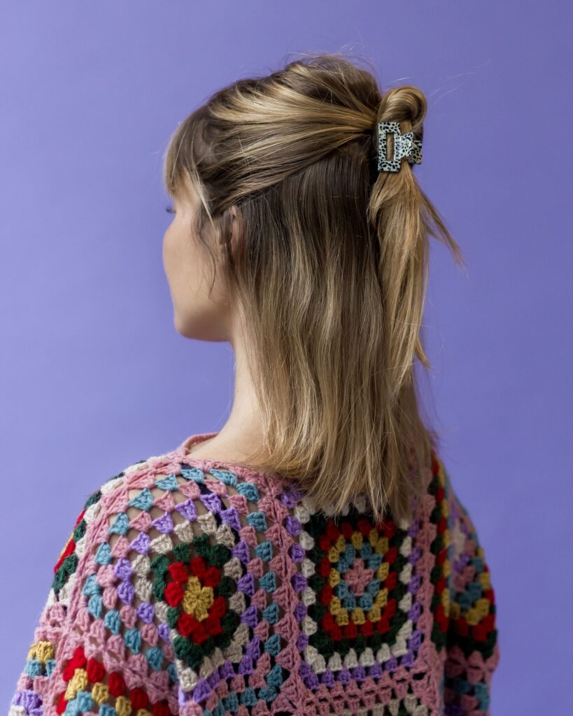 A woman with long straight blonde hair wears a half up mini bun secured with a small speckled black and white claw clip.