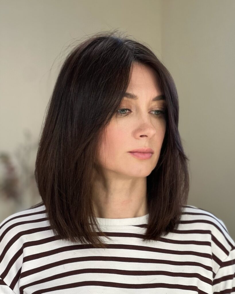 A woman with sleek, shoulder-length dark brunette hair and a soft center part.