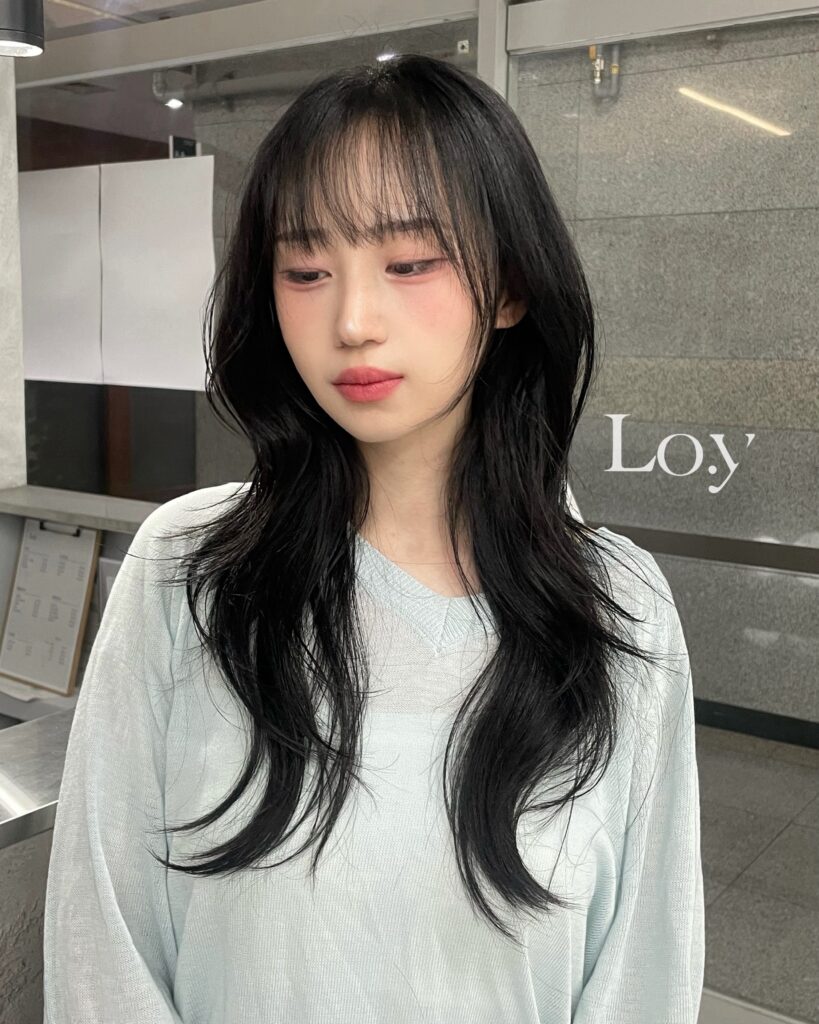 A woman with long jet black wavy layered hair and soft wispy bangs.