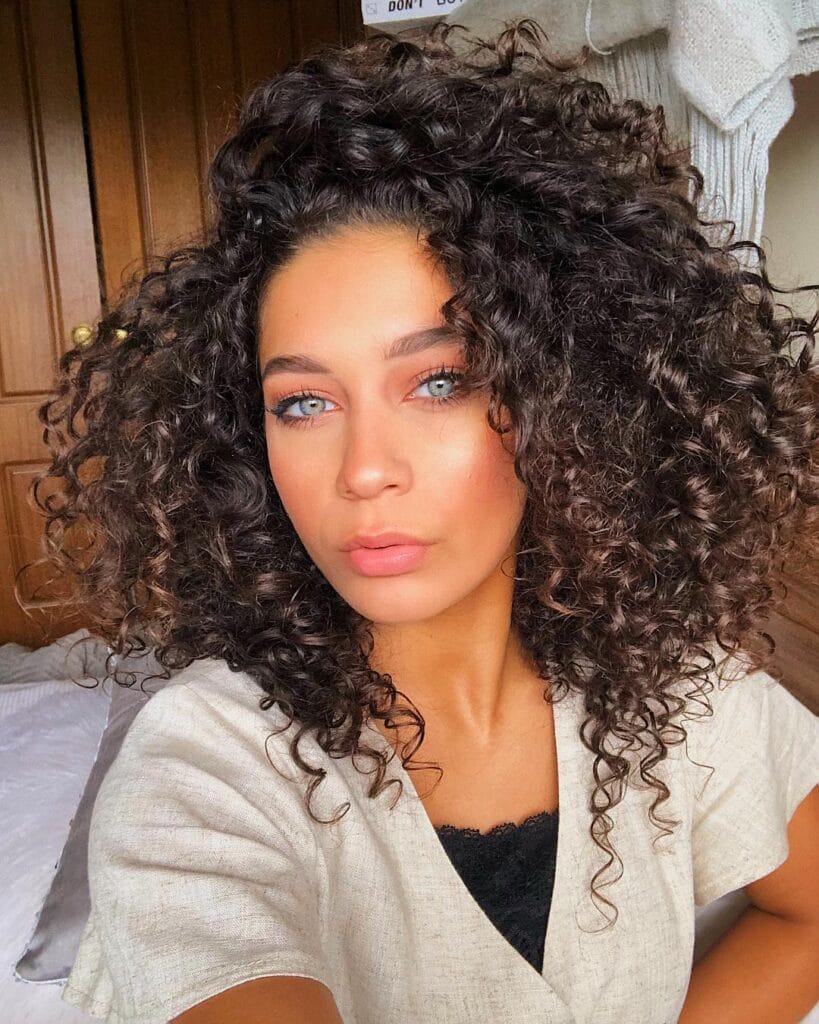 Mid length curly hairstyle with tight curls and high volume.