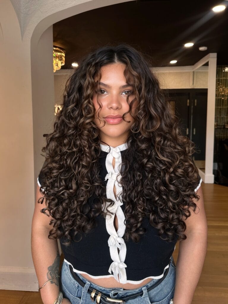 Long curly hairstyle with layered shape and defined curls framing the face.