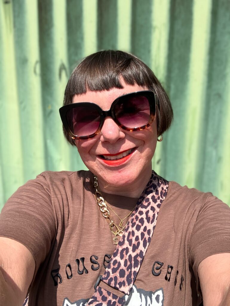 A woman with a sleek, ear-length, dark brown bob and a very short, straight micro fringe wearing sunglasses.