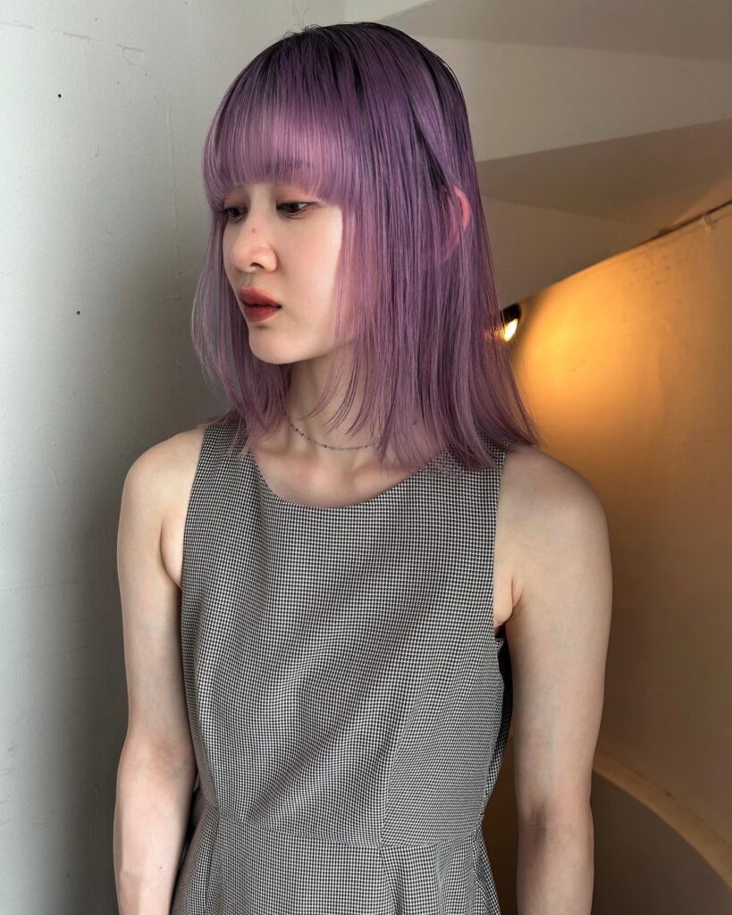 A woman with a sleek, straight lavender-purple long bob featuring heavy, blunt-cut bangs.
