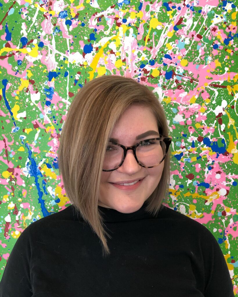 A woman with a straight, asymmetrical dirty blonde bob that is longer on one side.