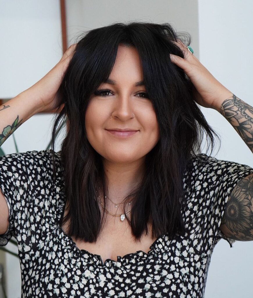 A woman with shoulder-length tousled black hair featuring choppy layers and soft middle-parted bangs.