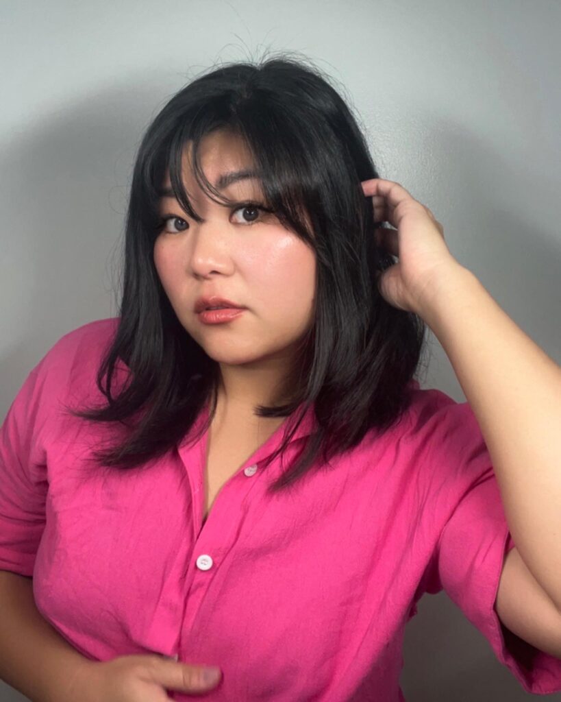 A woman with a shoulder-length black lob featuring soft waves and wispy see-through bangs.