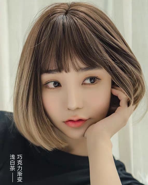 A woman with a smooth caramel ombre bob and light wispy bangs styled with a soft inward curve.