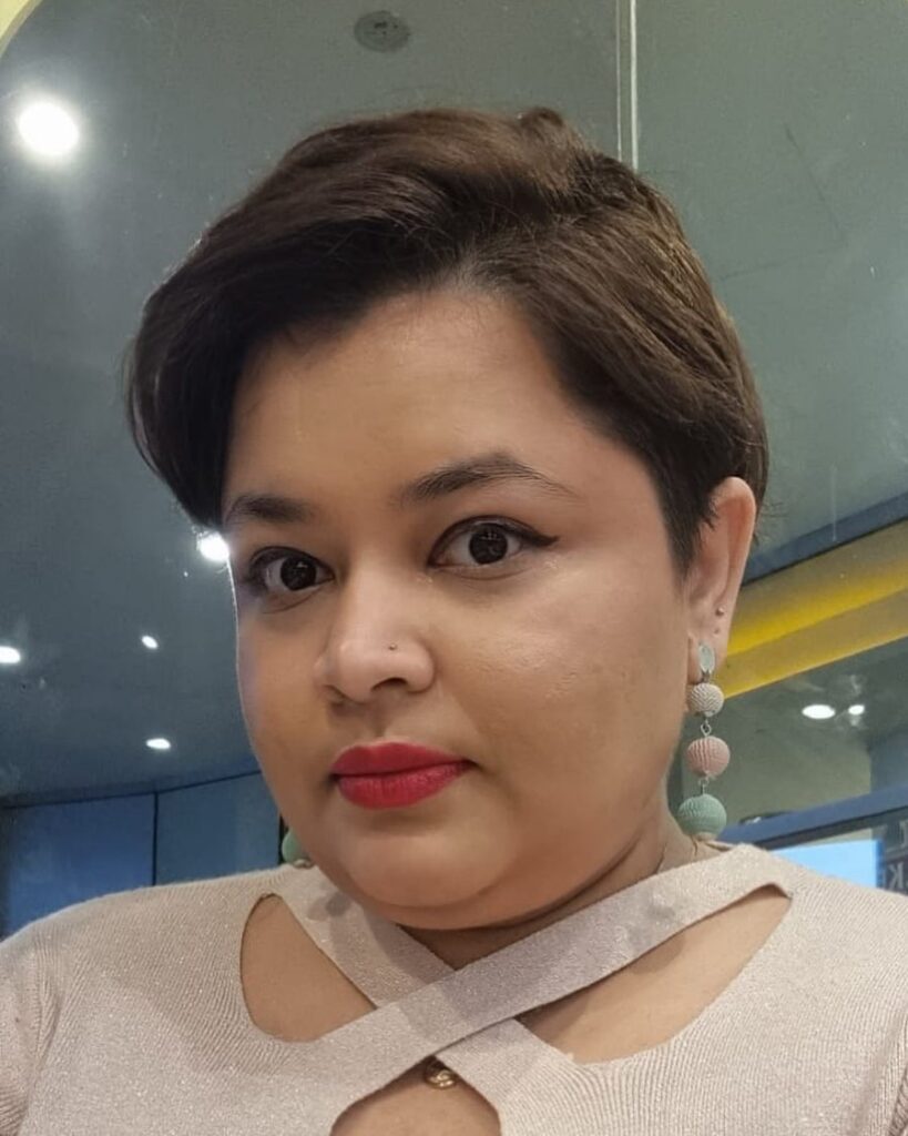 A woman with a short side-swept pixie cut in a rich brown color wearing colorful drop earrings.