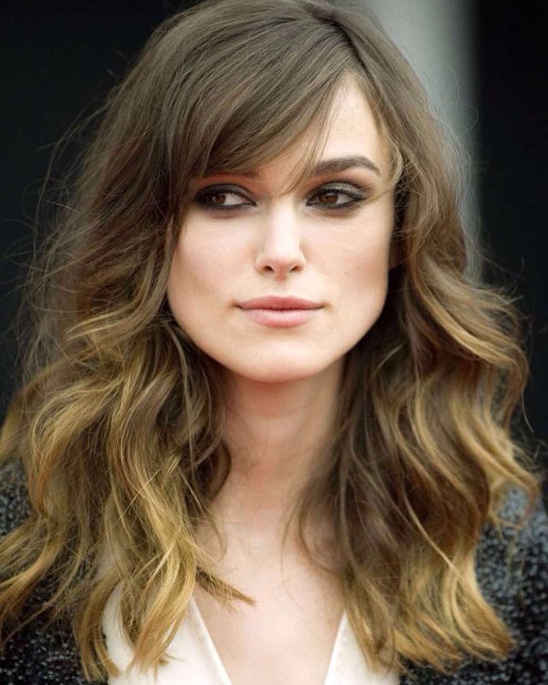Medium length wavy layered hair with side swept bangs and soft balayage color.
