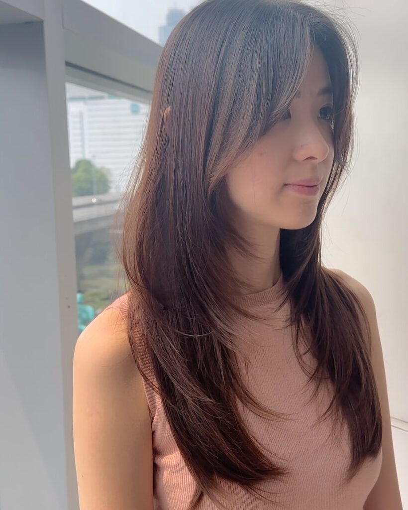 Mid length layered haircut with soft face framing bangs and a smooth brown finish.