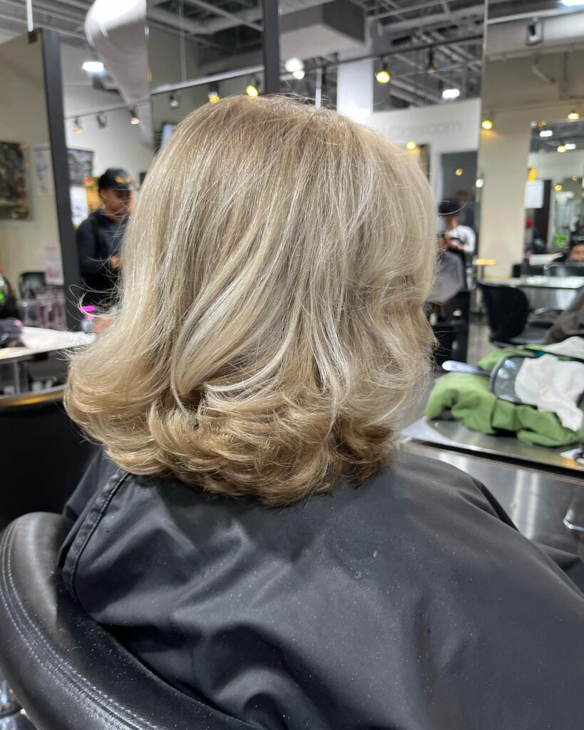A back view of a woman with mid-length honey blonde hair featuring voluminous layers and a bouncy blow-out.