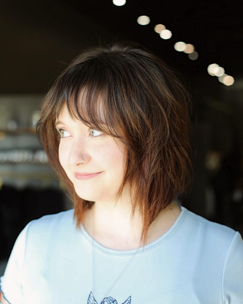 A woman with a texturized brunette bob featuring wispy bangs and choppy layers.