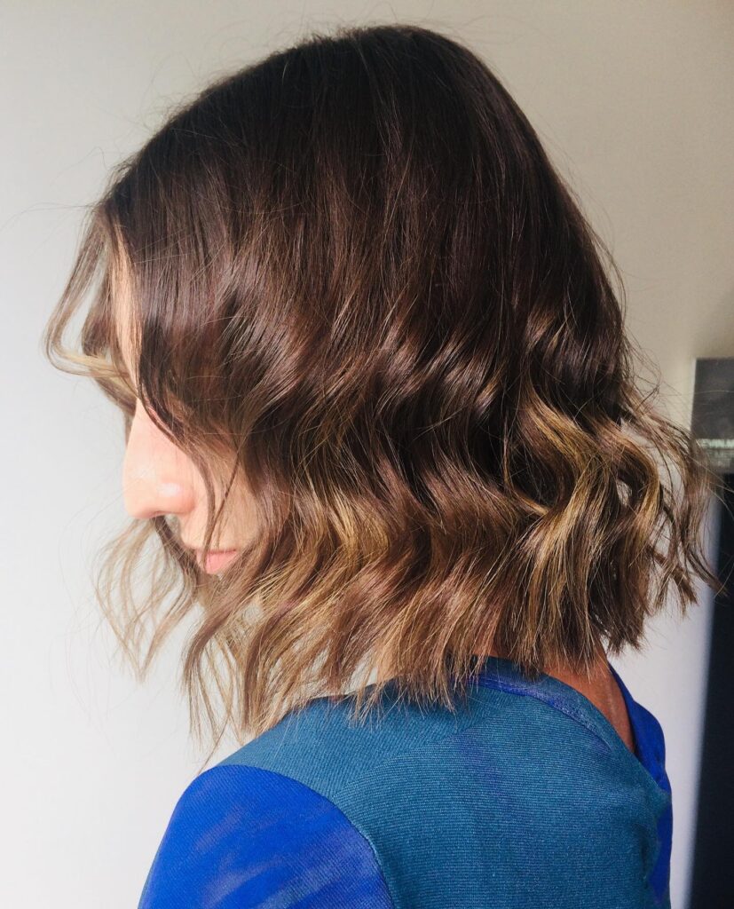 A woman with a shoulder-length chocolate brown bob with caramel balayage ends styled in loose waves.
