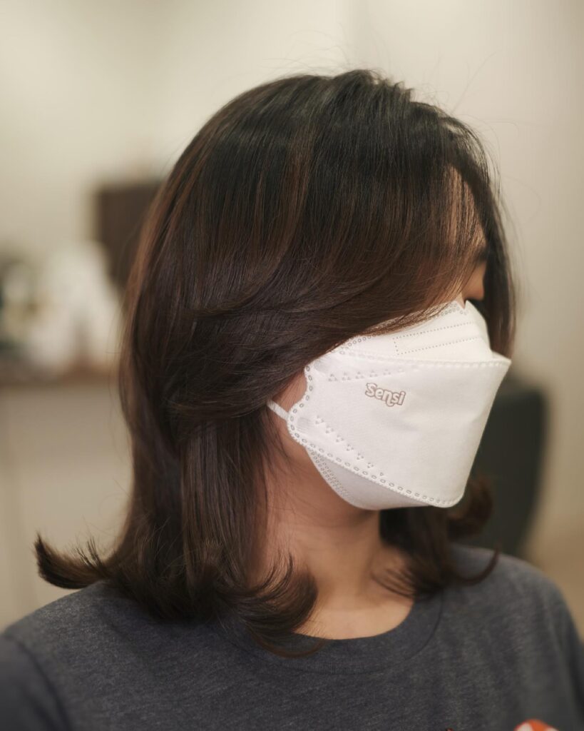 A woman with a mahogany brunette layered lob featuring long side-swept bangs and outward-curled ends.