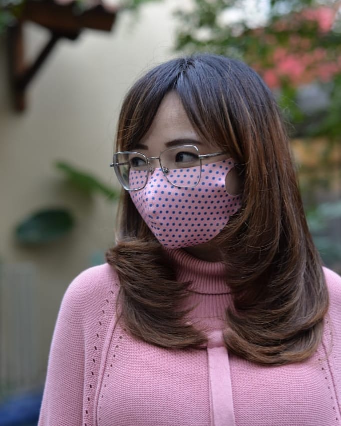 A woman wearing glasses and a pink sweater with medium-length brunette hair styled in sleek, rounded layers.