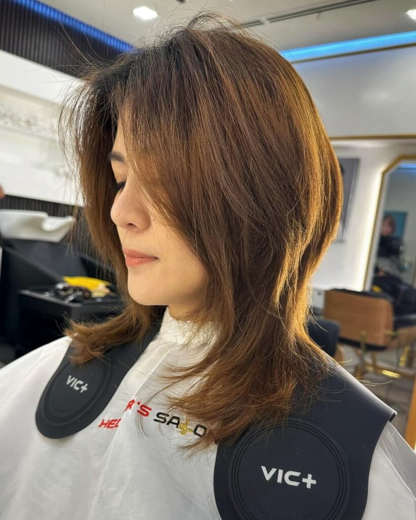 A woman with a medium-length chestnut brown shaggy butterfly haircut featuring voluminous layers and face-contouring ends.