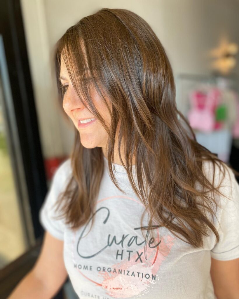 A woman with long chestnut brunette hair featuring wispy curtain bangs and soft textured layers.