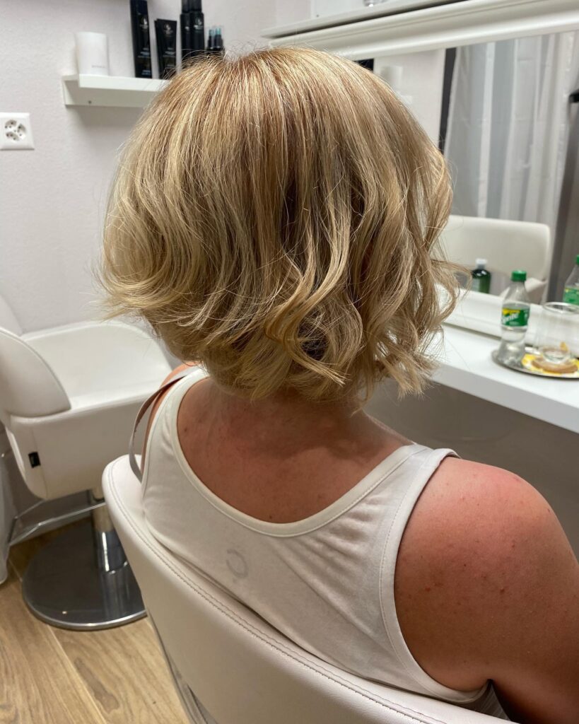 A back view of a woman with a neck-length champagne blonde bob styled in loose, tousled waves.