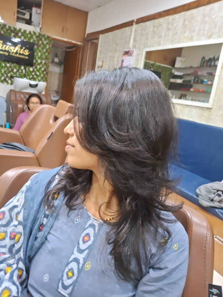 A woman in a salon with medium-length dark brunette hair featuring flippy, feathered layers and a side part.