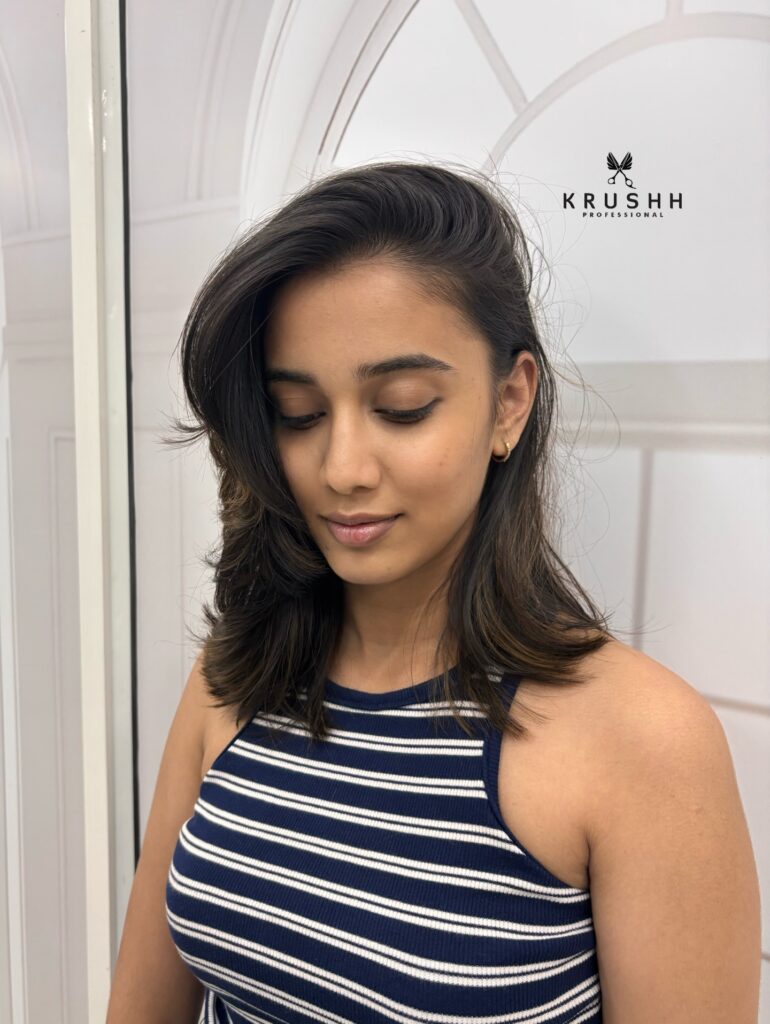 A woman with medium-length dark brunette hair styled with a deep side part and soft waves.