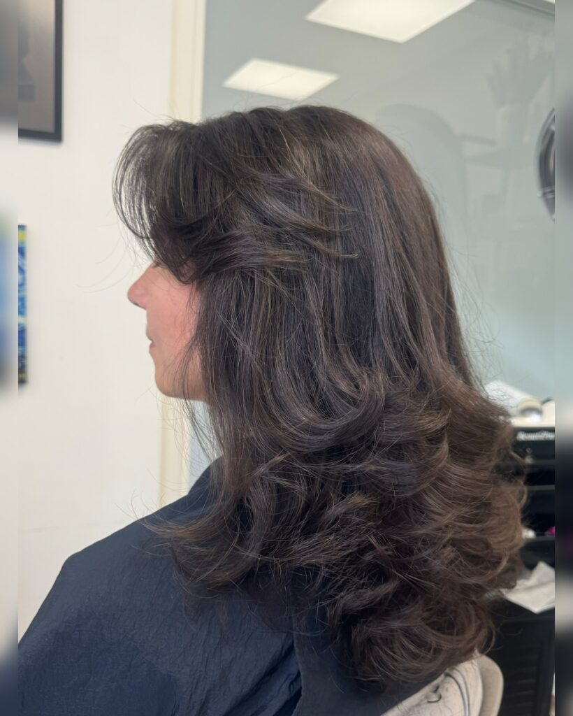 A woman with mid-length dark brown hair styled with voluminous feathered layers and bouncy curled ends.