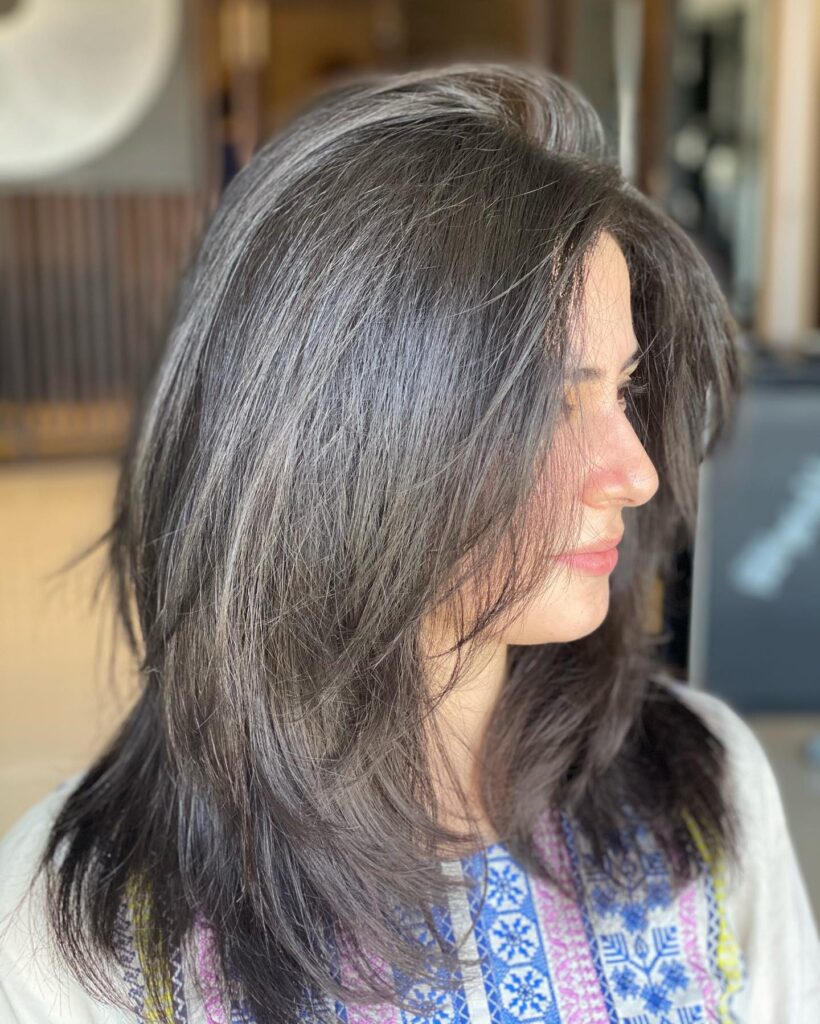 A woman with medium-length charcoal grey and brunette hair featuring feathered layers and a voluminous root lift.
