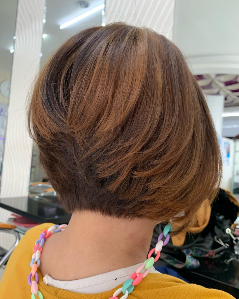 A back view of a woman with a steeply inverted caramel and brunette bob featuring stacked layers at the nape.
