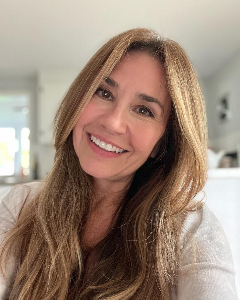 A smiling woman with long honey blonde hair featuring soft layers and a natural middle part.
