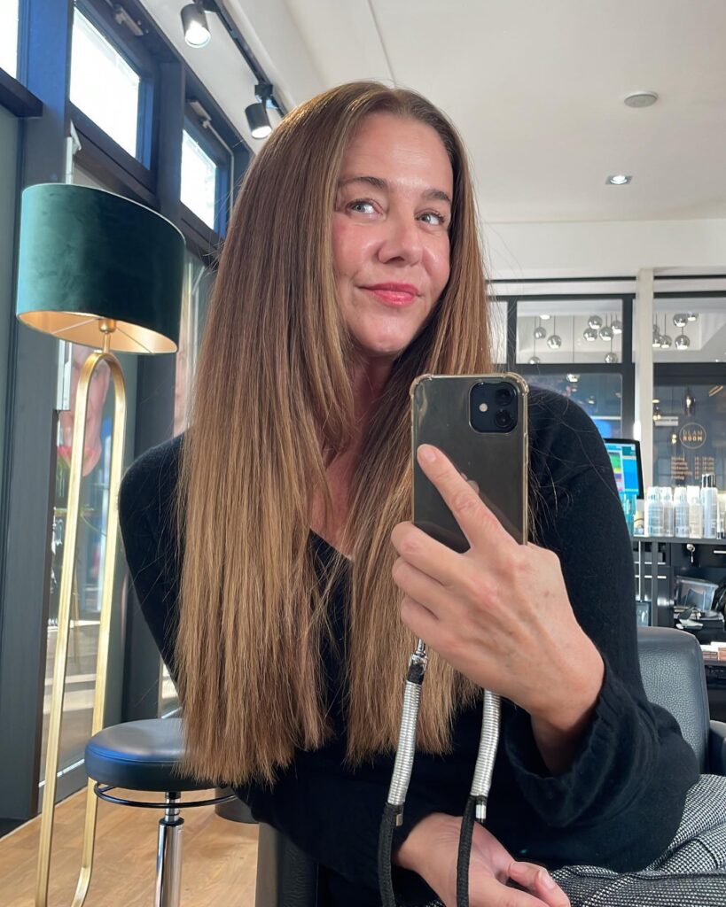 A woman with very long, straight caramel brunette hair featuring a middle part and a high-shine finish.