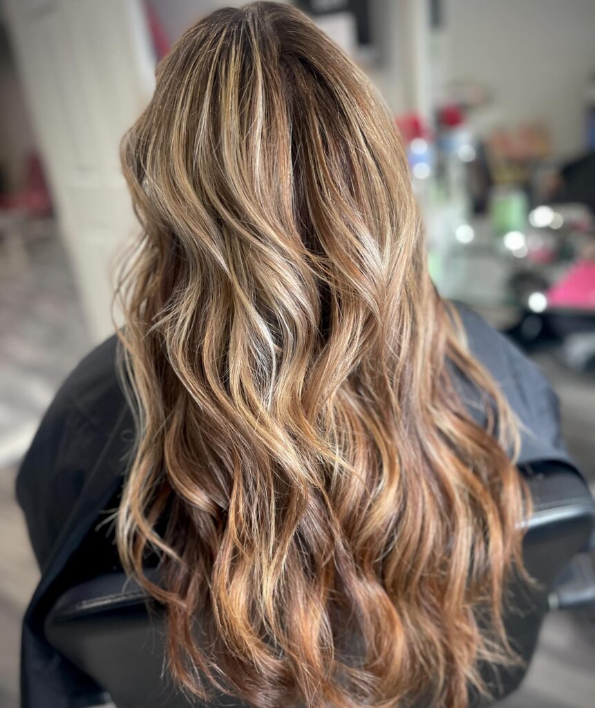 The back view of a woman with long wavy bronde hair featuring high-contrast blonde highlights and textured layers.