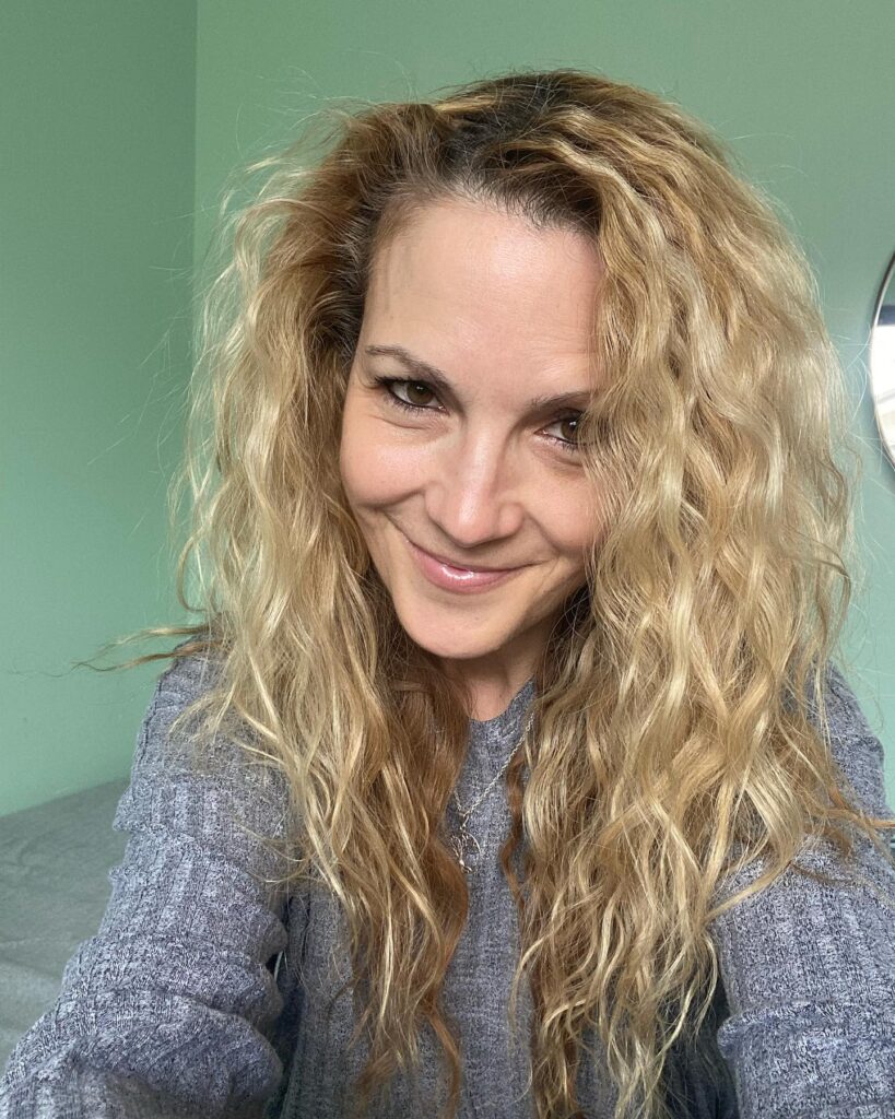 A smiling woman with long, messy golden blonde beach waves and lightly textured layers.