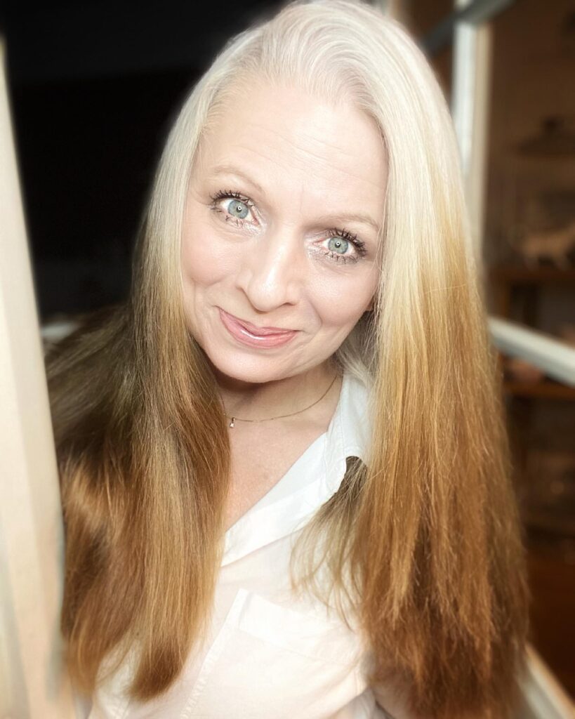 A woman with long straight hair featuring a transition from silver roots to honey-blonde ends.